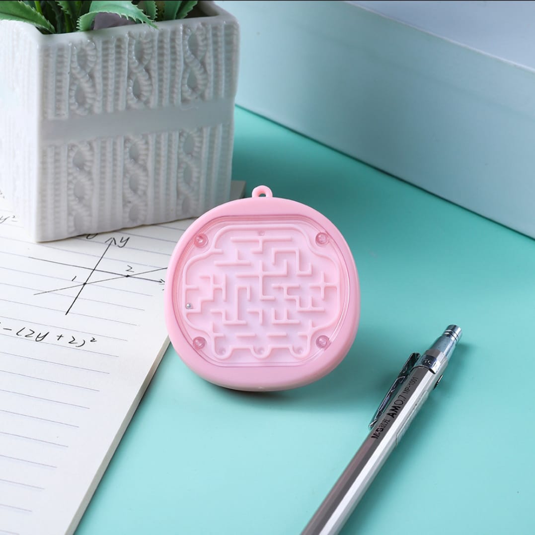 Pink maze-shaped object on a light blue surface with a pen and plant in the background